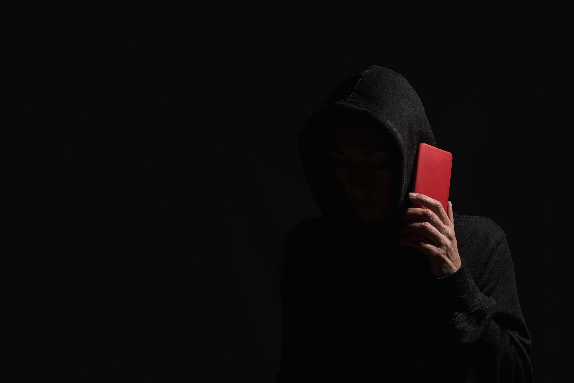 Hacker in black hood talking by smartphone in dark room for cyberattack and malware distribution