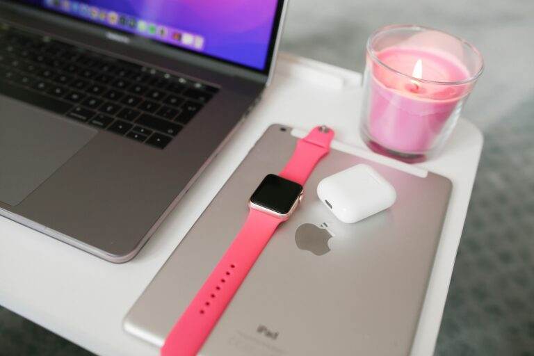 A neatly arranged desk with a laptop, iPad, smartwatch, AirPods, and candle.