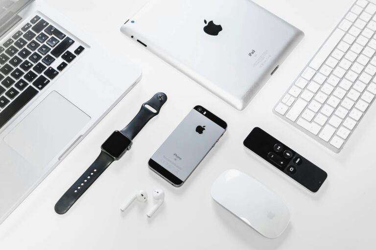 Flat lay of Apple devices including iPhone, iPad, MacBook, and Watch on a white surface, ideal for tech enthusiasts.