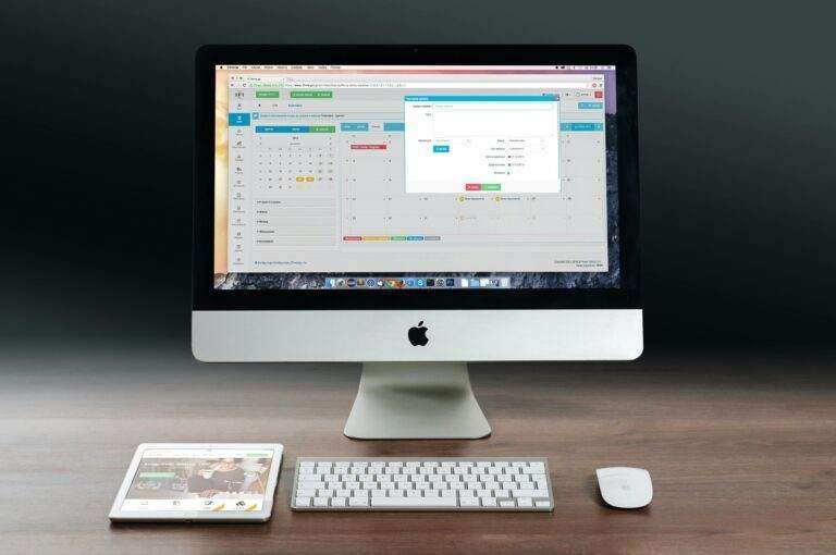 A sleek office setup featuring an Apple iMac, iPad, and keyboard on a wooden desk.