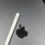 Apple intensifie ses échanges verbaux avec les régulateurs européens Close-up image of an Apple Pencil resting on a MacBook surface, showcasing technology accessories.