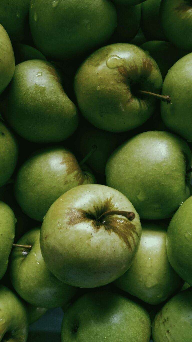 Tiny transparent drops on bunch of fresh green apples with short stems in daytime