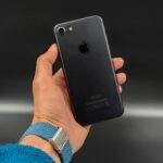 Close-up of a hand holding a black smartphone with a sleek design against a dark background.