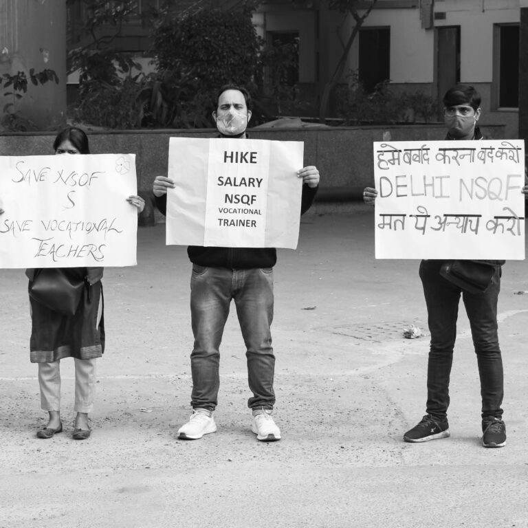 A group of adults hold signs in a black and white protest for vocational teacher rights.