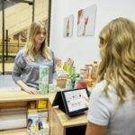 A woman pays at a checkout counter in a Berlin store, engaging with a cashier.