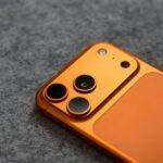 Stylish orange smartphone with triple camera lens on a gray fabric background, perfect for tech themes.