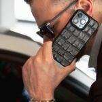 Close-up of a stylish man using a luxury iPhone with a leather case, indoors.