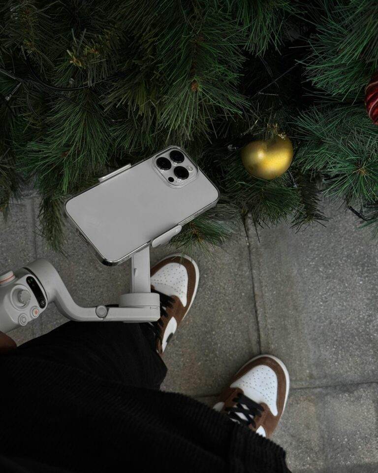 A smartphone on a gimbal captures a Christmas-themed scene with ornaments.