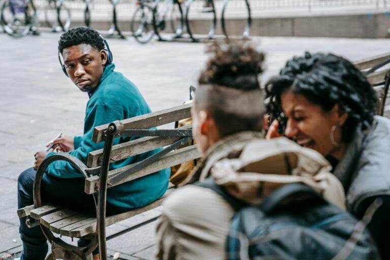 A diverse group of young adults engage in conversation on a street bench.