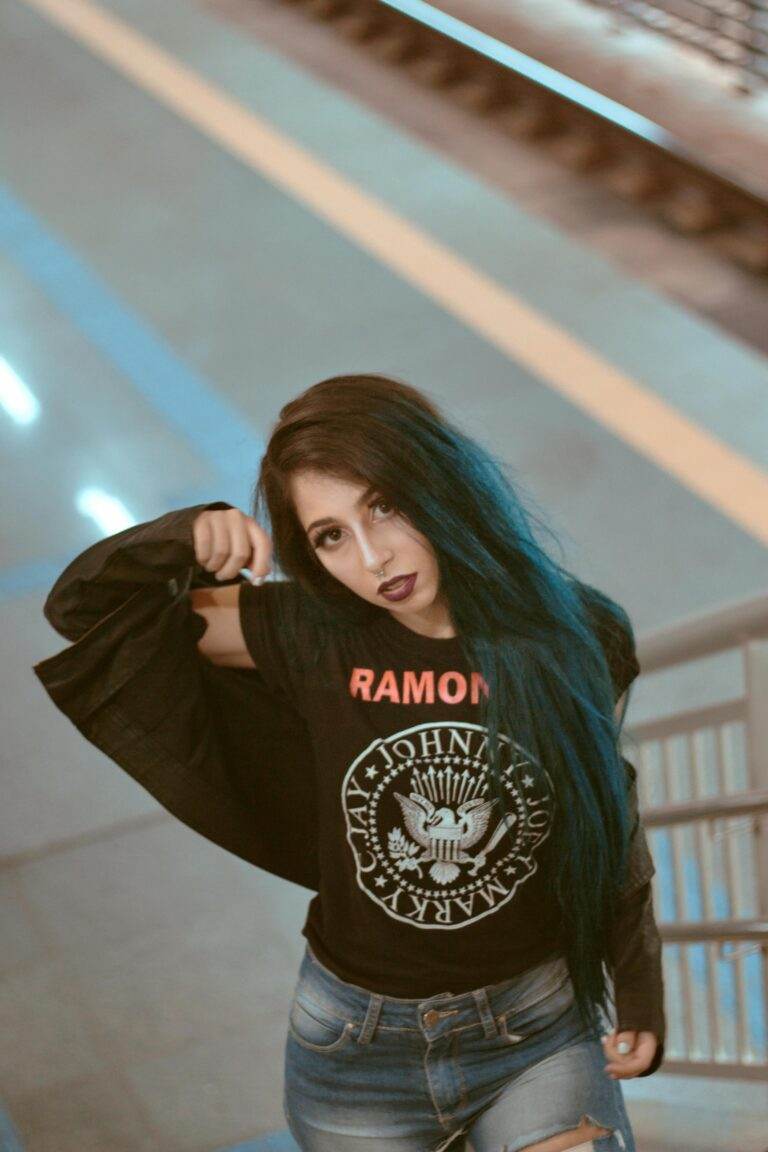 Portrait of a fashionable woman with blue hair wearing a Ramones T-shirt in an urban environment.