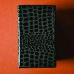 Close-up of a textured black leather box on a vibrant orange background, showcasing elegance and style.