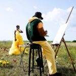 Artist painting a model in a yellow dress outdoors with flowers in Lagos, Nigeria.