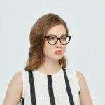 Portrait of a young woman wearing glasses, in a stylish striped dress, against a plain background.