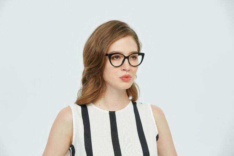 Portrait of a young woman wearing glasses, in a stylish striped dress, against a plain background.