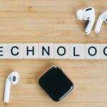 Pebble Round 2 : Le retour tant attendu de la montre connectée classique, réservations ouvertes dès maintenant Flat lay of wireless earphones and smartwatch next to TECHNOLOGY tiles on a wooden table.