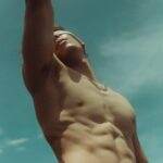 Décès de Steve Hayden, l'écrivain emblématique du célèbre spot publicitaire '1984' d'Apple, à l'âge de 78 ans Shirtless man reaching upwards under a clear summer sky, showcasing fitness and freedom.