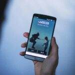 Person holding a smartphone displaying a music app login screen in focus.