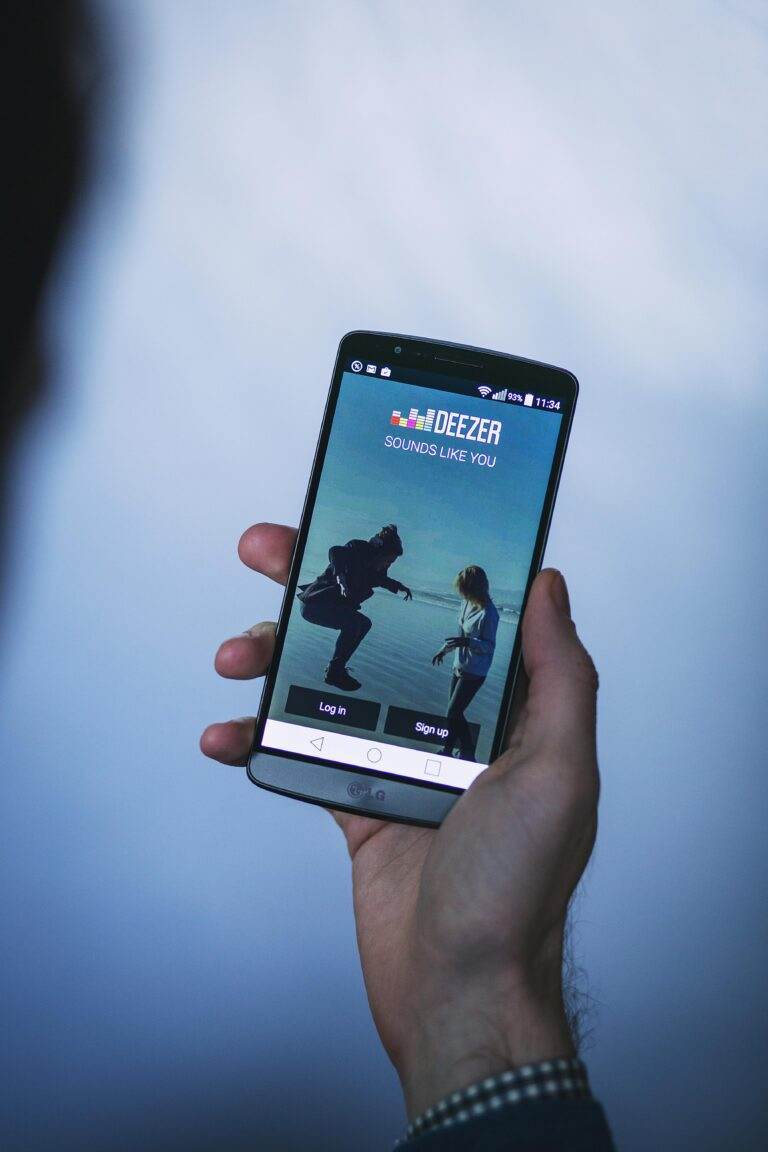 Person holding a smartphone displaying a music app login screen in focus.