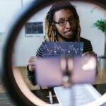 Eddy Cue d’Apple refuse la stratégie des géants du streaming : « Non à un Apple TV+ façon Netflix ou Disney+ » A vlogger reviews cryptocurrency stock charts in a modern setting with a ring light.