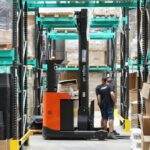 Warehouse scene featuring workers and a forklift navigating aisles for logistics and inventory management.