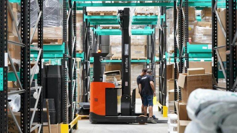 Warehouse scene featuring workers and a forklift navigating aisles for logistics and inventory management.