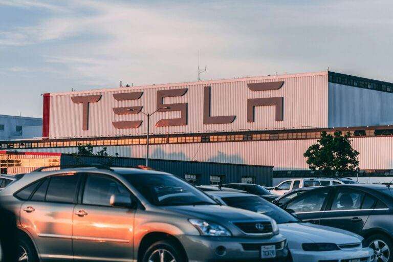 Tesla en quête d’intégration : vers un support d’Apple CarPlay dans ses véhicules Tesla factory with parked cars during sunset, showcasing modern automotive industry vibes.