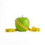 A vibrant green apple encircled by a yellow measuring tape, set against a clean white background.