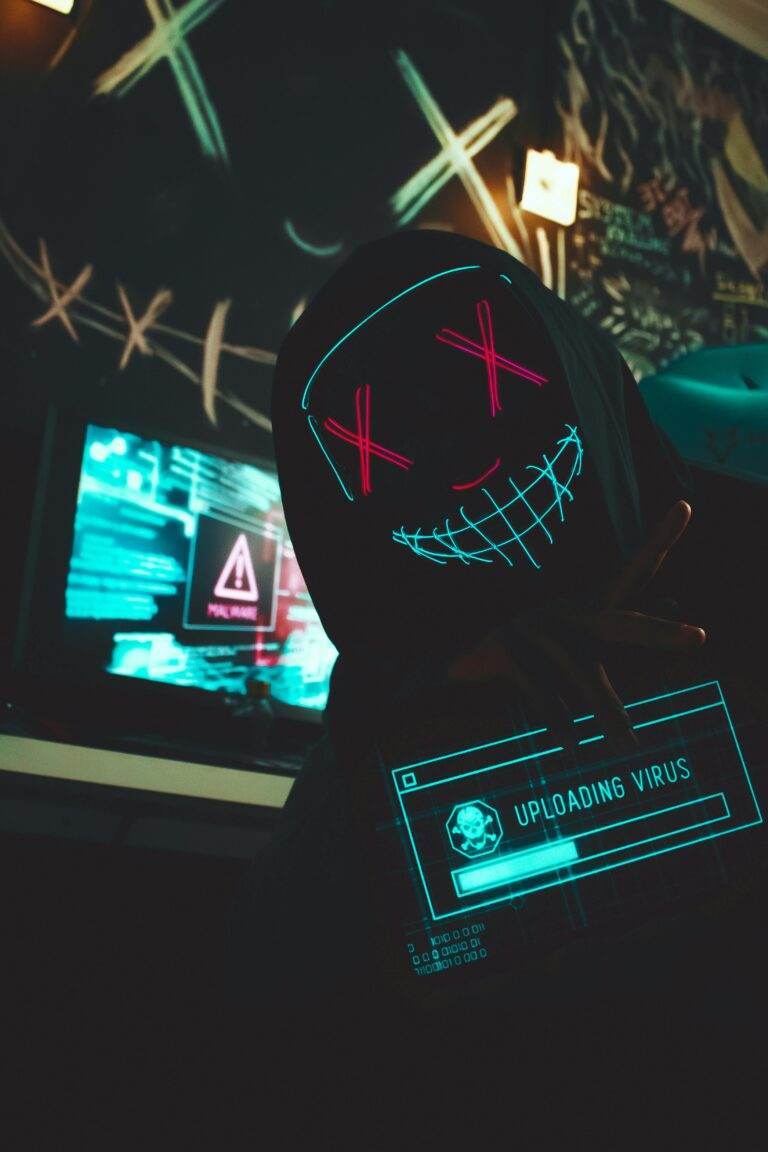 Smishing : quand un simple SMS peut anéantir votre vie numérique A hacker in a mask uploads a virus from a dimly lit room filled with computer screens.