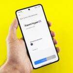 Hand holding smartphone showing Xiaomi HyperOS update screen on yellow background.
