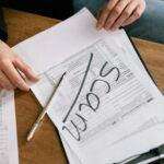 Close-up of hands on tax form with 'scam' written, highlighting tax fraud.