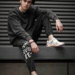 Young adult sitting on ledge in trendy attire with modern urban backdrop.