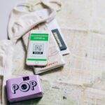 Flat lay of travel essentials including a passport, map, smartphone, and pop camera.