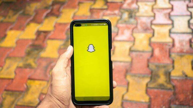 Comment supprimer définitivement son compte Snapchat A person holds a smartphone displaying the Snapchat logo against a colorful brick background.