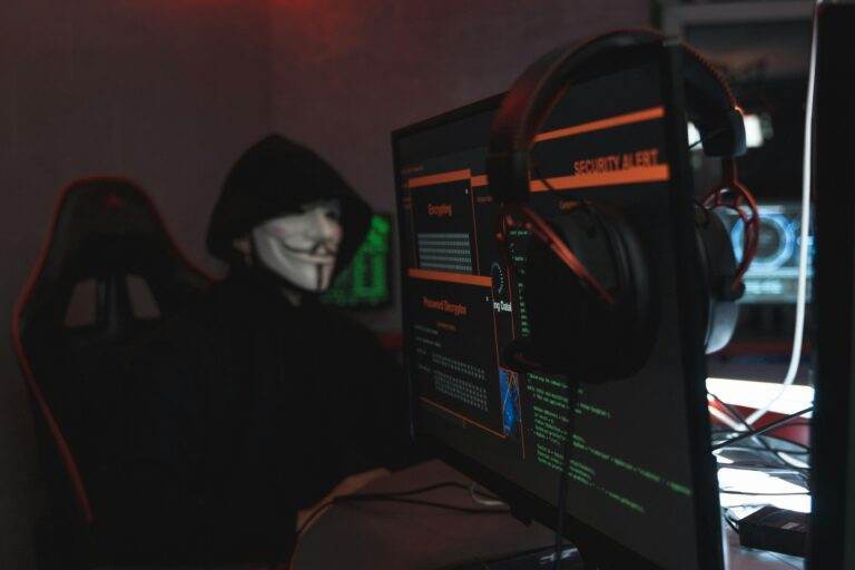 A person wearing a Guy Fawkes mask engaged in hacking activities on a computer in a dimly lit room.