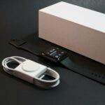 Quand MacRumors réinvente le cadeau tech : cette sélection 2025 va changer votre façon d'offrir A modern smartwatch with charger displayed elegantly alongside its packaging on a dark surface.