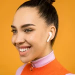 Comment Choisir Les Meilleurs AirPods Apple Pour Vous (Et Éviter Cette Erreur Cruciale Close-up portrait of a young woman with airpods, styled in a bun against an orange background.
