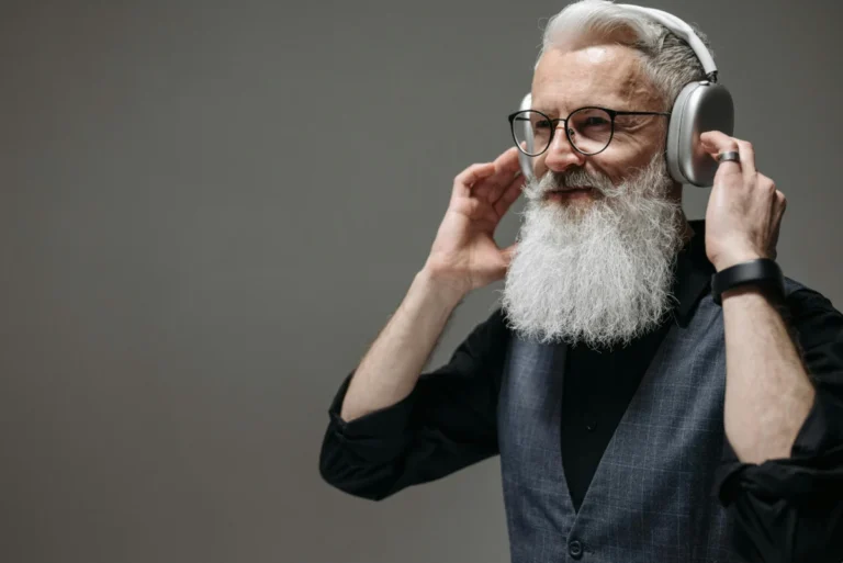 Mature man with white beard wearing wireless headphones and smiling in a studio setting.