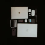 Top view of modern apple electronics including laptops, smartphone, and accessories on a dark background.