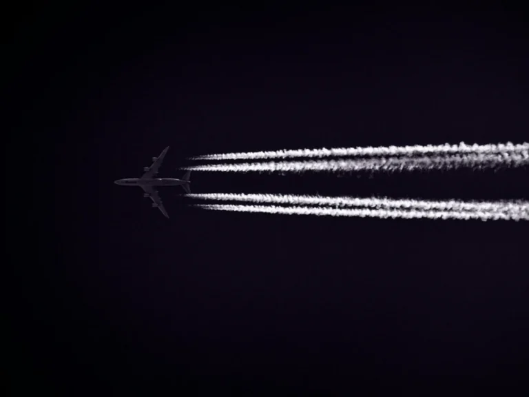 A jet airplane leaves contrails as it flies through the night sky, showcasing modern aviation technology.