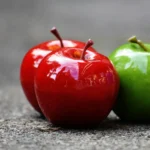 Close-up of shiny red and green apples on a textured surface, showcasing freshness and vibrant colors.