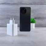 Minimalist composition of a smartphone, charger, and small green plant on a grey background.