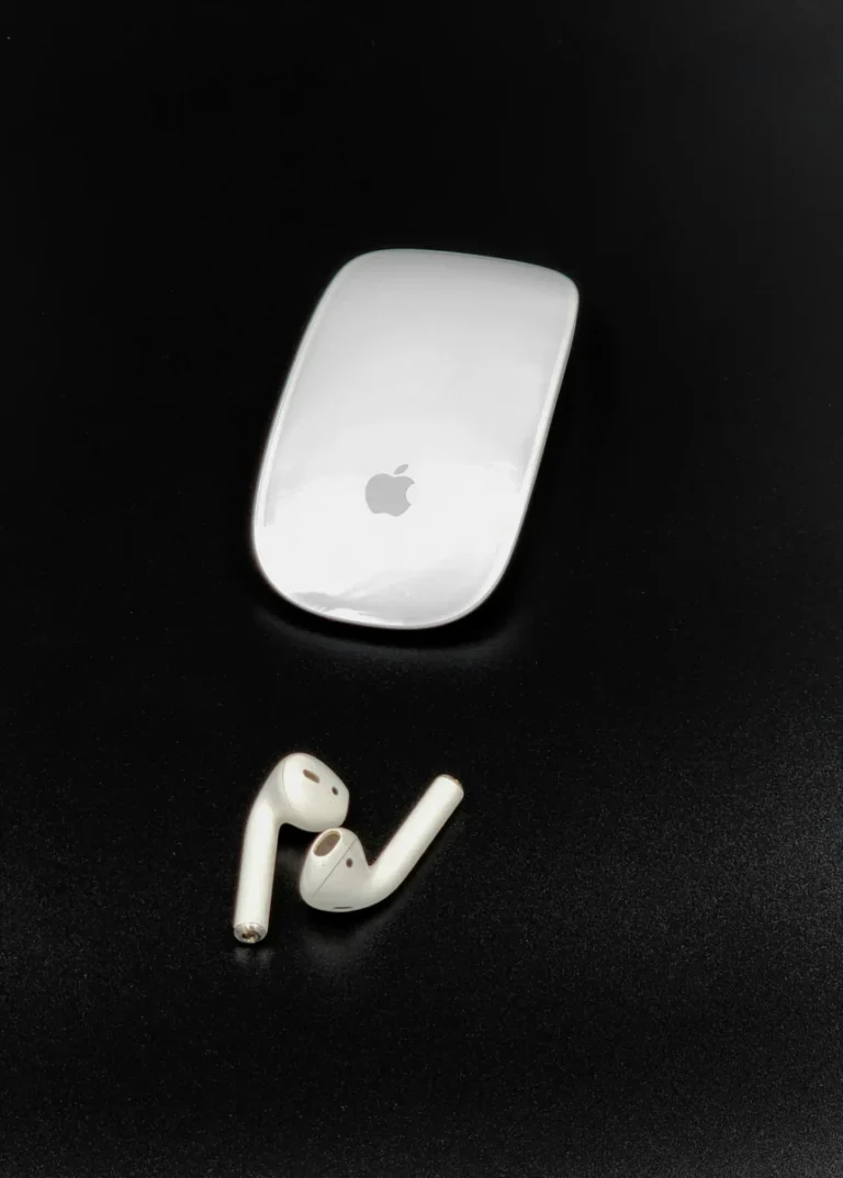 Close-up of an Apple Magic Mouse and AirPods on a sleek black background.