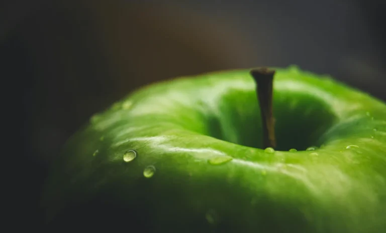 Detailed close-up of a fresh green apple with water droplets in soft light, showcasing its texture.