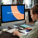 A woman at a desk using a computer and tablet in a modern home office.