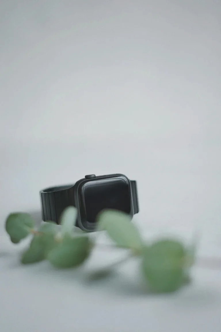 Sleek black smartwatch on a white background with green leaves, showcasing modern technology.