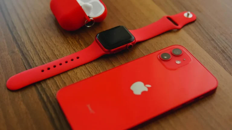 Close-up of red Apple iPhone, smartwatch, and AirPods on wooden table.