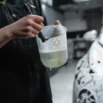 Close-up of person using brush and soap for car detailing in a garage.