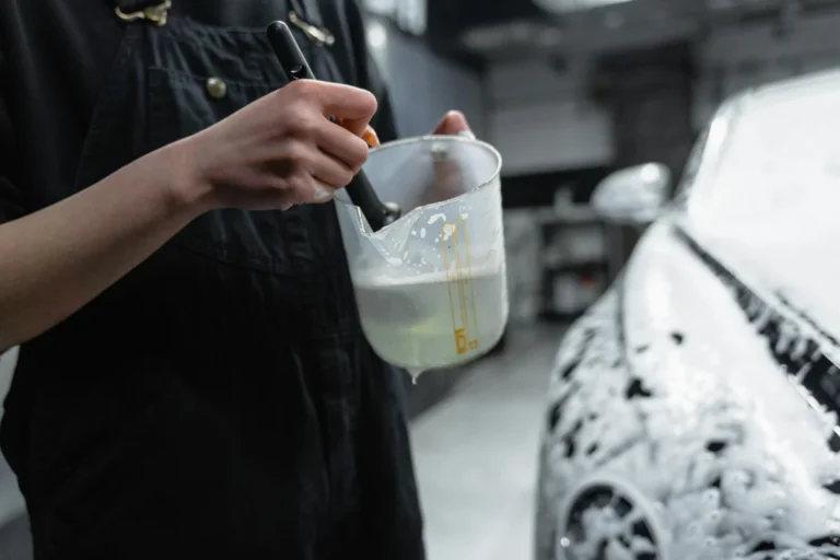 Close-up of person using brush and soap for car detailing in a garage.