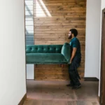 Berkshire Hathaway réduit sa participation dans Apple et acquiert des actions du NYTimes dans les derniers mouvements de Buffett en tant que PDG A mover carries a green sofa indoors, showcasing modern interior design and relocation services.