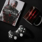 La nouvelle série cyberpunk d’Apple TV : l’adaptation d’un roman « infréquentable » qui a révolutionné le genre Flat lay of The Witcher Wild Hunt game with controller and themed mug on black background.
